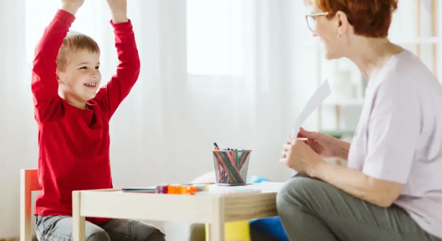 Chłopiec z podniesionymi rękami, uśmiechnięty, podczas sesji terapeutycznej. Może to być pomocne w ocenie objawów ADHD u dzieci test.