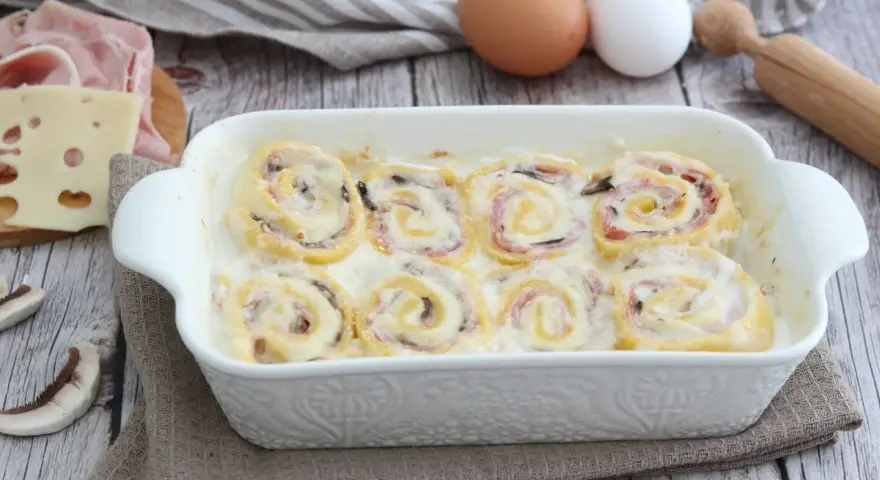Nidi di rondine in una teglia bianca, con prosciutto, formaggio e funghi. Ingredienti per un piatto delizioso.
