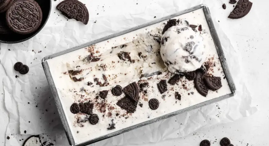 Cremiges Oreo Eis in einer Metallform, garniert mit ganzen und zerbrochenen Keksen. Ein Löffel Eis liegt obenauf.