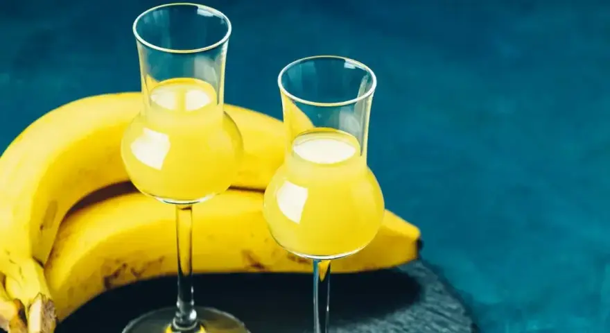 Dwa kieliszki z żółtym likierem bananowym obok dojrzałych bananów. Idealny przepis na domowy likier bananowy.