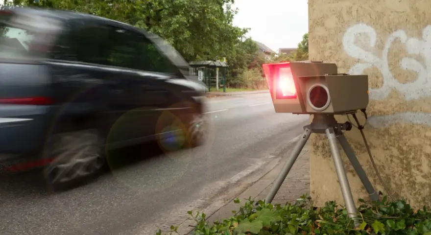 Ein Blitzer, der gerade ein Auto fotografiert, wie sehen Blitzer ohne Blitz aus? Dieses Gerät steht am Straßenrand, bereit für Geschwindigkeitsünder.