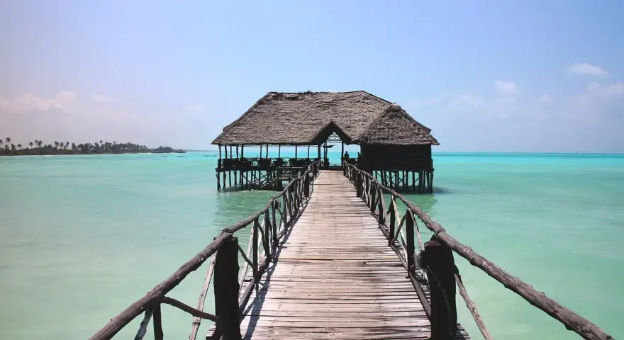 Drewniany pomost prowadzi do chatki na palach na turkusowej wodzie. Idealne miejsce na wiza zanzibar.