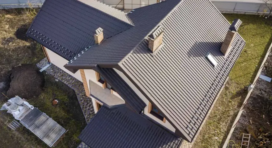 Dachówka na dachu domu, z widocznym kominem, który przypomina rzygownik.