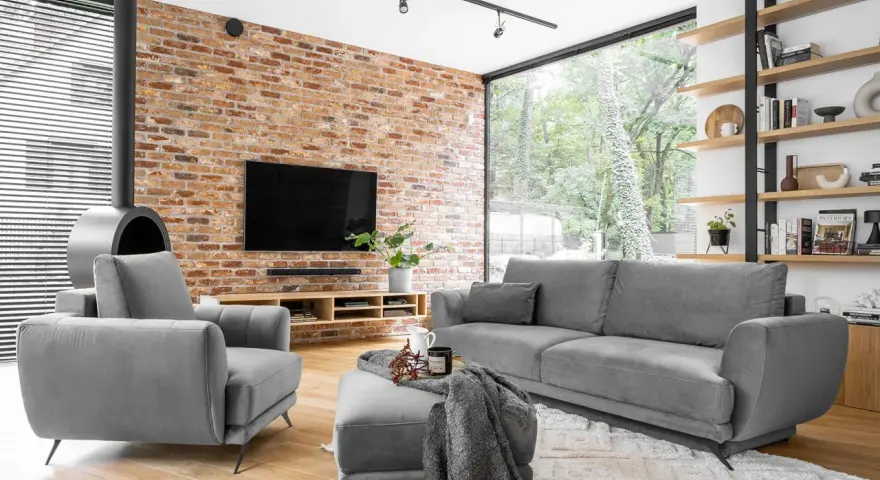 Nowoczesne, szare komplety wypoczynkowe z funkcją spania Black Red White. Wygodna sofa i fotel przy ceglanej ścianie.