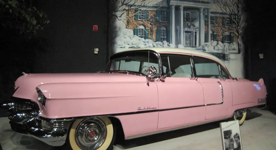 Ein rosafarbener Cadillac, der einst Elvis Presley gehörte, steht vor einer gemalten Kulisse von Graceland.