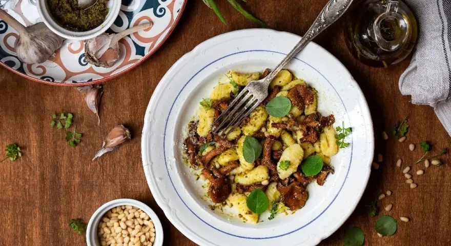 Szybkie danie z gnocchi z grzybami i pesto, posypane orzeszkami pinii. Idealne na szybki obiad.