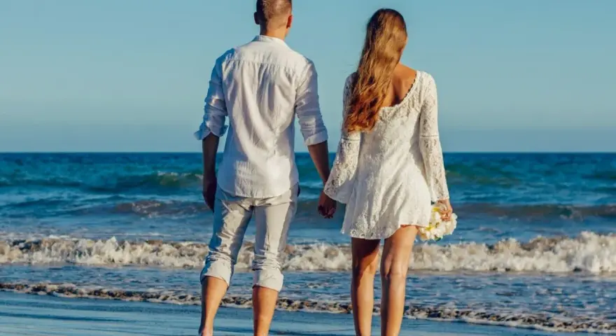Para idąca plażą, trzymająca się za ręce. Ich miłość grecka kwitnie na tle błękitnego morza i nieba.