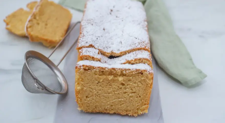 Puszysty makaron z mąki migdałowej, oprószony cukrem pudrem, czeka na spróbowanie. Obok leżą dwa kawałki ciasta i sitko.