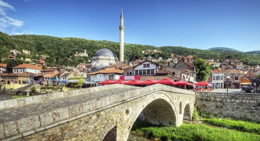 Kamienny most nad rzeką, z widokiem na meczet i miasto na wzgórzu. Kosowo atrakcje turystyczne zachwycają.