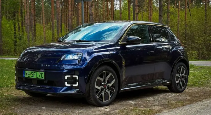 Ciemnoniebieski Renault 5 E-Tech elektryczny stoi na drodze leśnej.