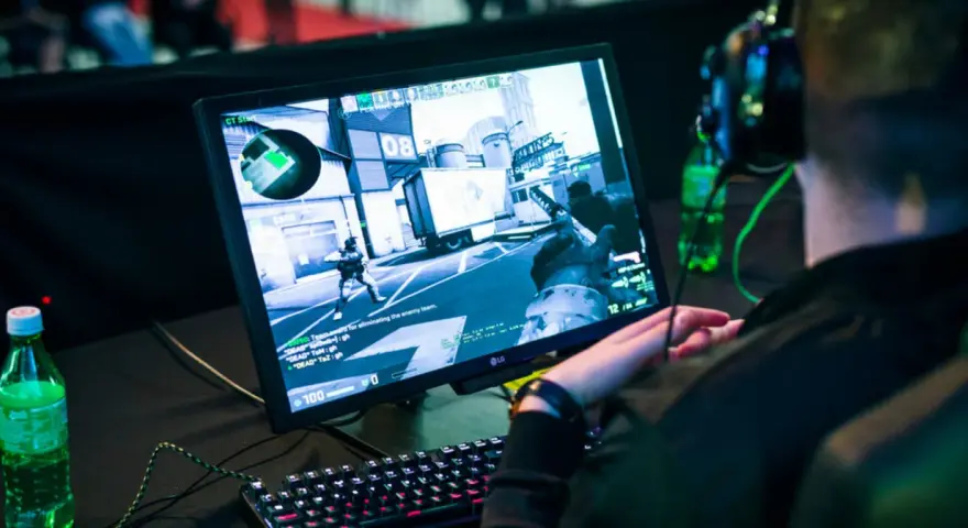 Gracz w słuchawkach gra w CS:GO, próbując jak zmniejszyć ping. Na ekranie widać akcję z gry i klawiaturę.