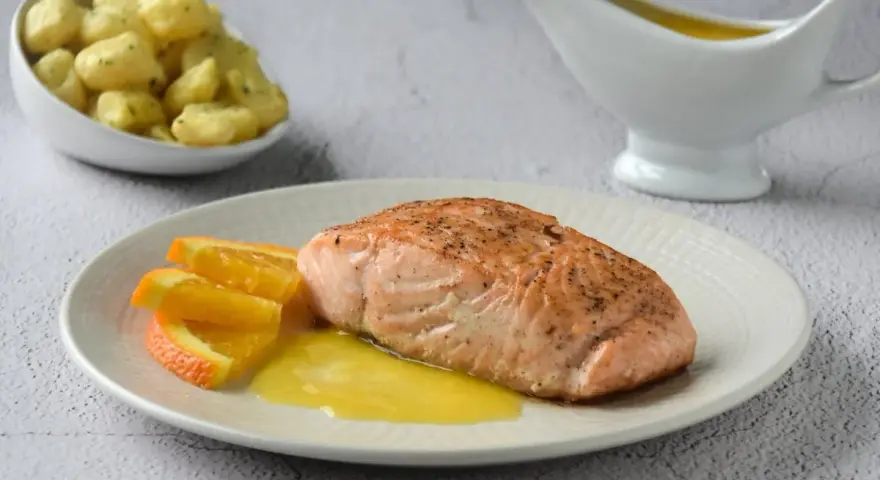 Filete de salmón a la naranja, servido con gajos de naranja y una salsa dorada. Acompañado de patatas pequeñas.