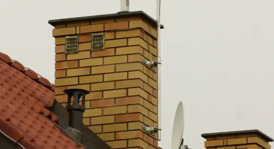 Dwa kratkowane otwory wentylacyjne na ceglanym kominie, zapewniające odpowietrzenie kanału sanitarnego.
