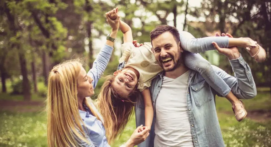 Glückliche Familie im Park. Vater trägt Tochter auf den Schultern, Mutter hält ihre Hände. Kein Anzeichen von Einzelkind-Syndrom, nur pure Freude.