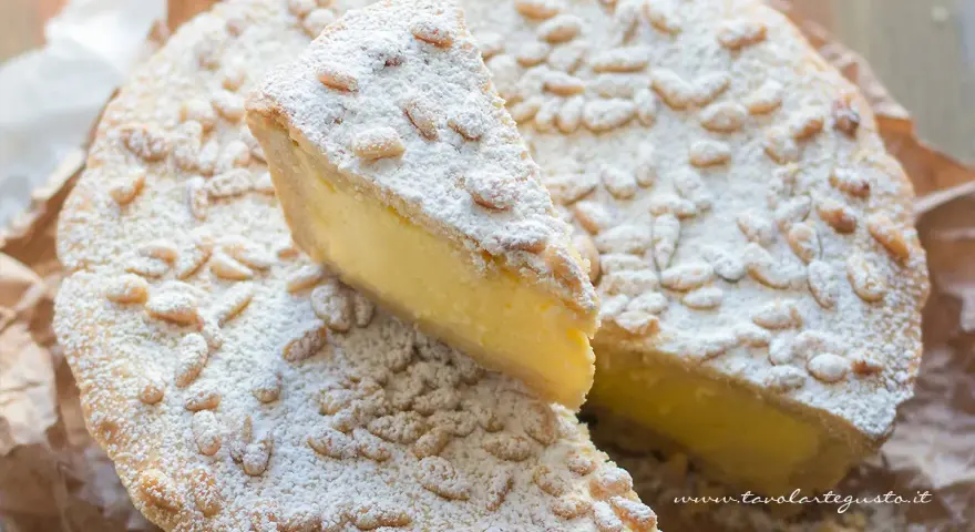 Una fetta di torta della nonna, ricca di crema e cosparsa di pinoli e zucchero a velo, pronta per essere gustata.