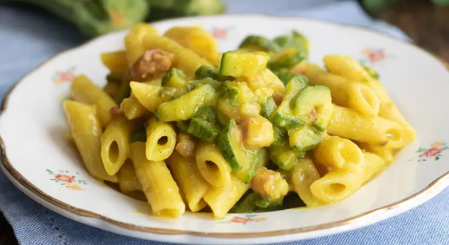 Piatto di pasta penne con zucchine a rondelle e cubetti di pancetta croccante, condita con una salsa cremosa.
