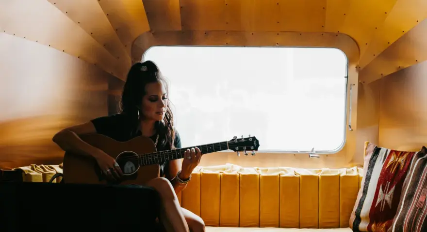 Sarah Jones, piosenkarka, gra na gitarze w przytulnym wnętrzu.