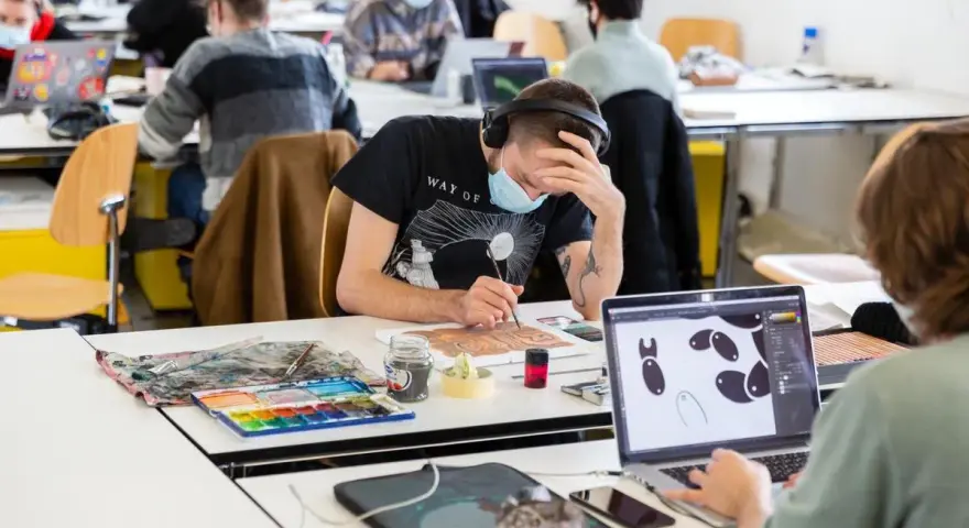 Des étudiants concentrés dans une école d'art, certains peignent, d'autres travaillent sur ordinateur. L'ambiance est studieuse.