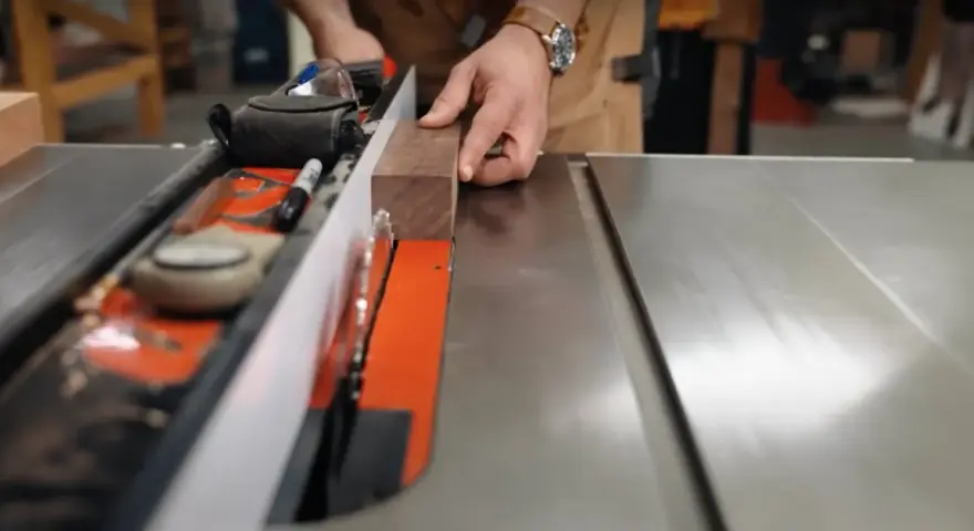 Hands guide a wooden plank along a table saw's fence, demonstrating how to use a table saw for precise cuts.