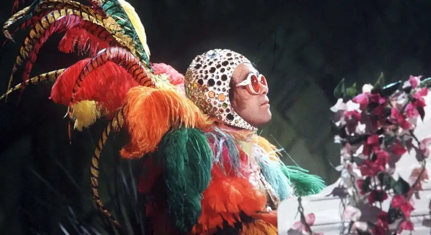 Elton John in einem extravaganten Federkostüm, das an einen Pfau erinnert. Seine ikonischen Elton John Outfits sind legendär.