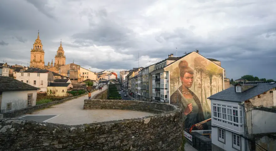 Mural de mujer en edificio, con la muralla romana y la catedral al fondo. Imprescindible que ver en Lugo.