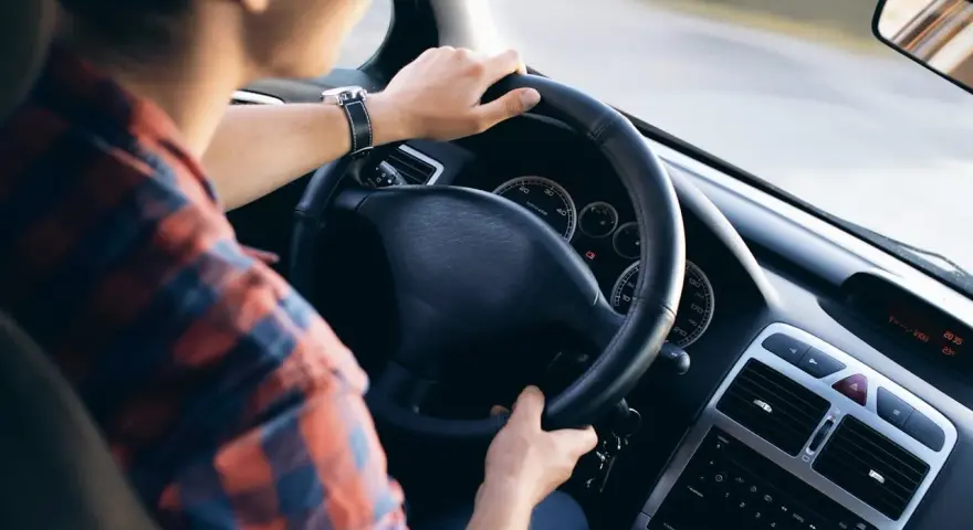 Mężczyzna w kratę prowadzi samochód, wiedząc jak jeździć po wymianie oleju. Na desce rozdzielczej widać zegary i radio.