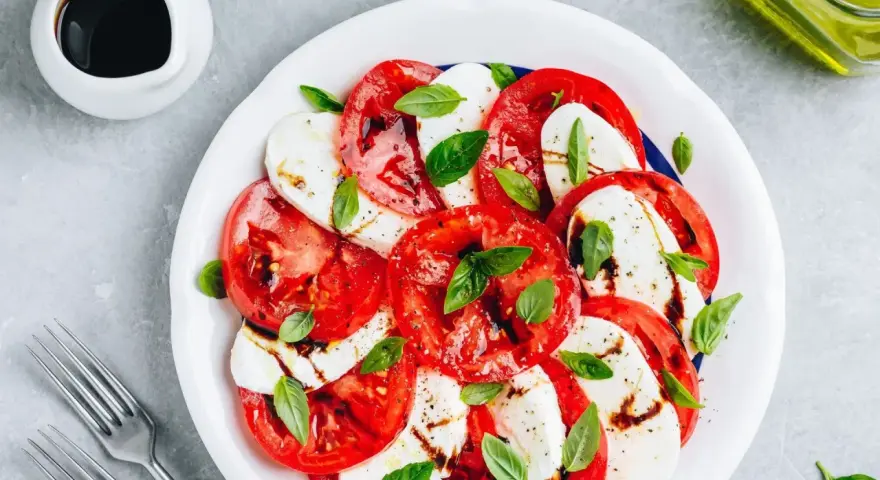 Pyszna sałatka caprese z pomidorów, mozzarelli i bazylii, polana sosem balsamicznym.