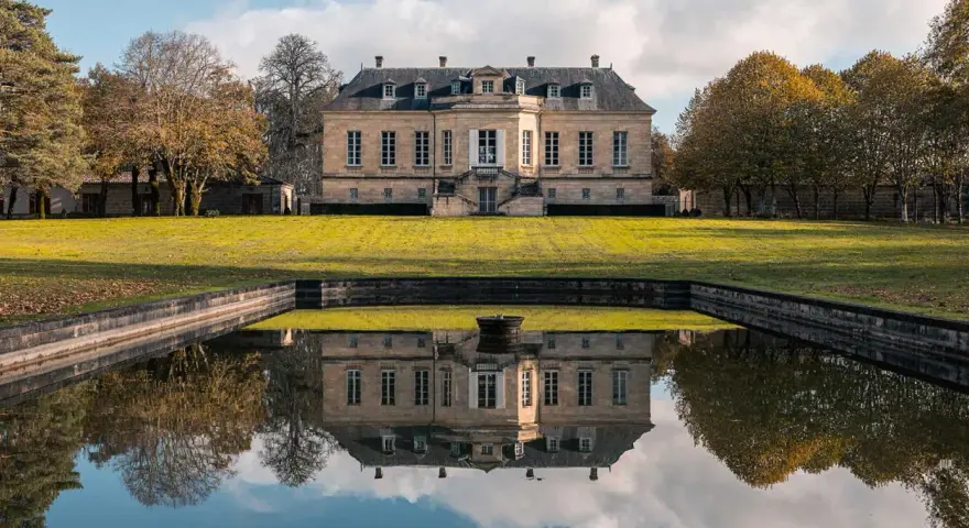Le château La Louvière, majestueux, se reflète dans un étang paisible, entouré d'arbres aux couleurs d'automne.