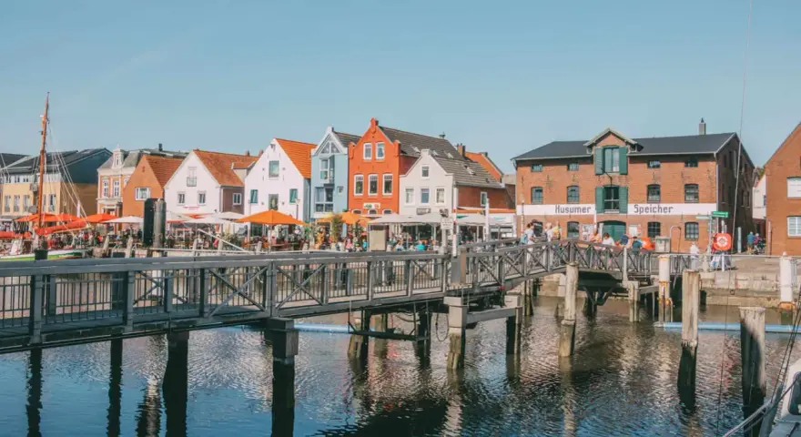 Bunte Häuser am Hafen, ein Steg führt über das Wasser. Perfekt für Ausflüge in Husum, mit Cafés und dem alten Speicher.