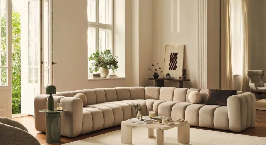 Ampio divano componibile color crema, dalle forme morbide e arrotondate, perfetto per definire le dimensioni di un salotto moderno.