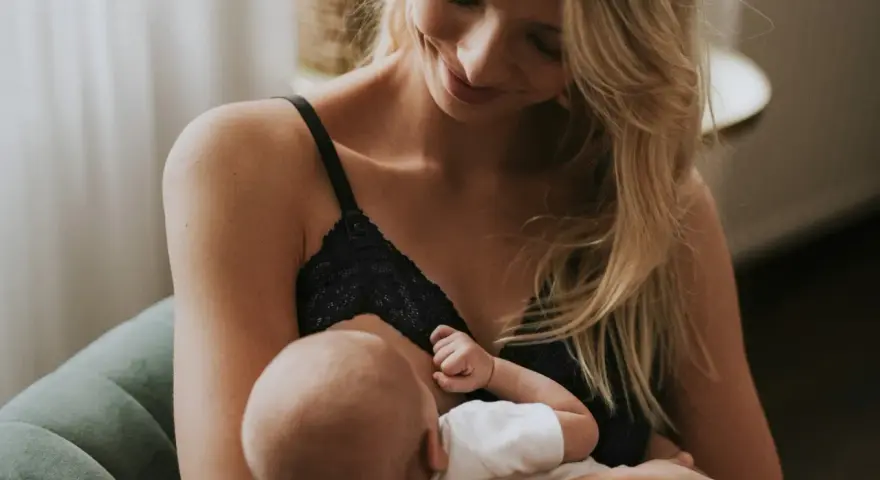 Uśmiechnięta mama karmi piersią swoje dziecko. Delikatne chwile bliskości i miłości.