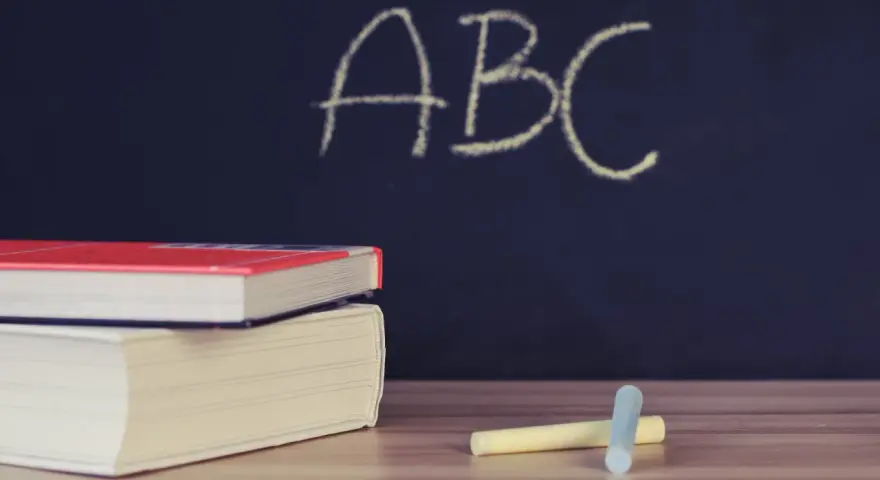 Libri e gessetti su un tavolo di legno, con la scritta "ABC" su una lavagna scura. Un'immagine che evoca l'inizio di nuovi percorsi di apprendimento, come i **corsi abilitanti**.