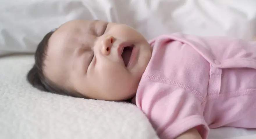 Ein süßes neugeborenes Baby in rosa Strampler niest. Die Augen sind geschlossen, der Mund leicht geöffnet.