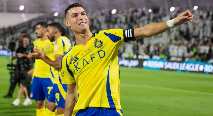 Uśmiechnięty Cristiano Ronaldo w żółtej koszulce Al Nassr, świętujący sukces. Jego zarobki w Arabii Saudyjskiej budzą podziw.