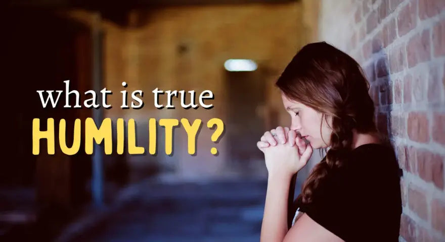 A woman with her hands clasped in prayer leans against a brick wall, contemplating "what is true HUMILITY?".