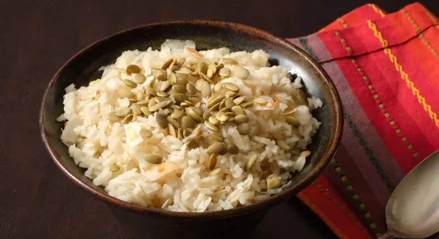 Un tazón de arroz de coco con semillas de calabaza y coco rallado, servido sobre una servilleta colorida.