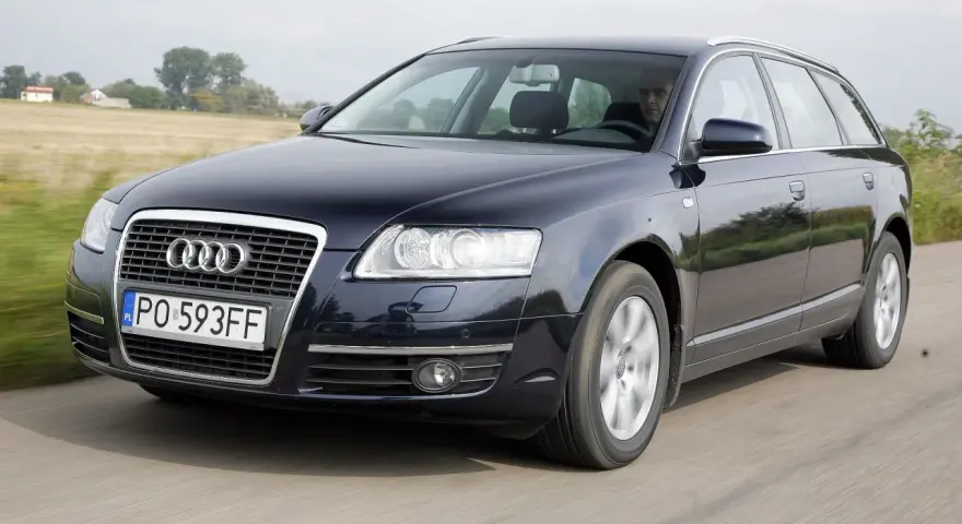 Ciemnogranatowe Audi A6 C6 3.2 FSI Avant w ruchu. Kierowca za kierownicą. Wady tego modelu mogą dotyczyć np. układu napędowego.