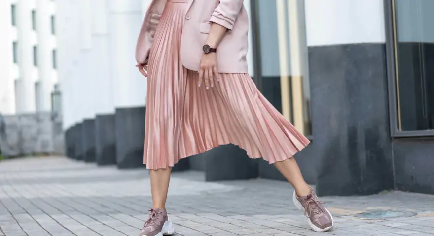 Kobieca stylizacja: różowa plisowana spódnica, marynarka i sportowe buty. Idealne połączenie elegancji i wygody, pokazujące, jakie buty do plisowanej spódnicy pasują najlepiej.
