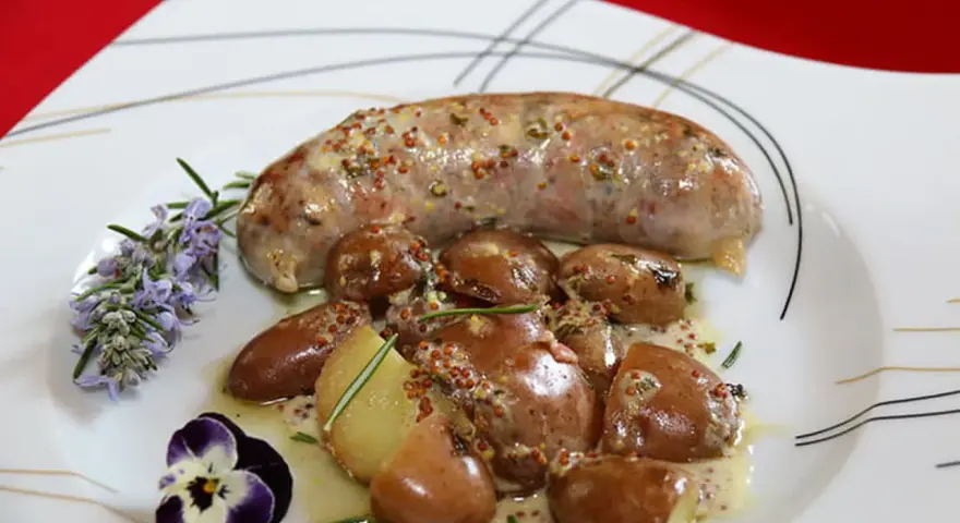 Une andouillette sauce moutarde, accompagnée de pommes de terre grenaille et garnie de romarin et d'une pensée.