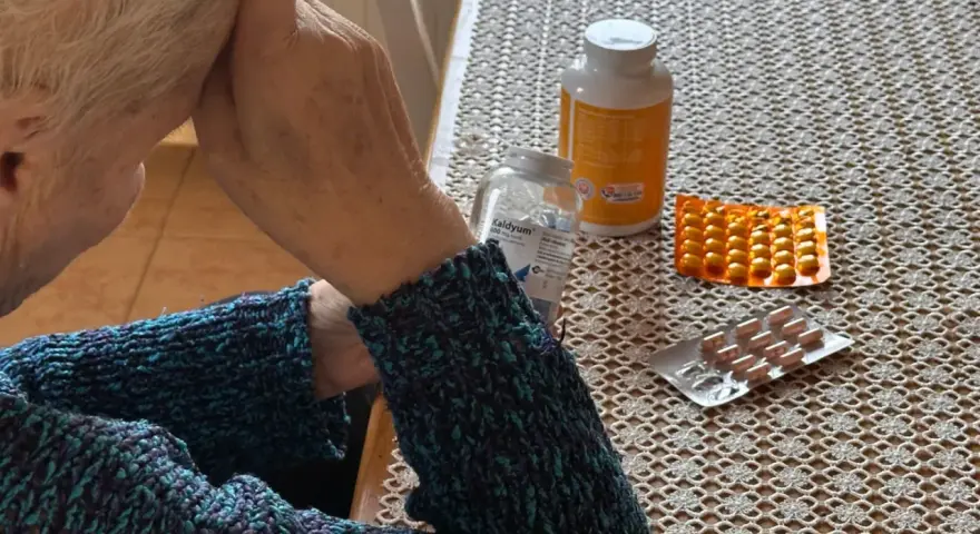Starsza pani z lekami na stole, zastanawia się nad emeryturą po mężu i nowymi zasadami.