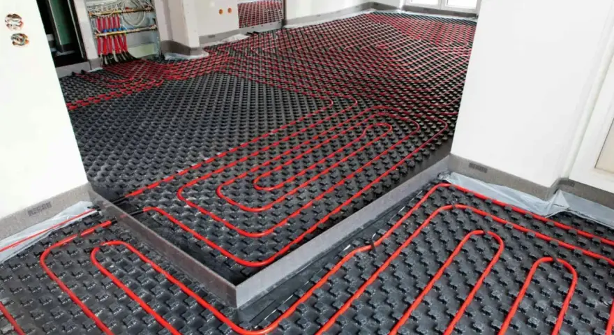Instalación de un sistema de calefacción por suelo radiante, con tuberías rojas serpenteando sobre una base negra. Preparando un suelo refrescante para el confort.