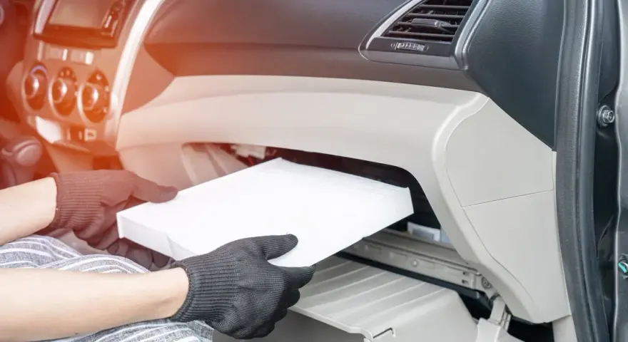 Wymiana filtra kabinowego w Audi A3 8L. Ręce w rękawiczkach wyjmują biały filtr z wnętrza schowka.