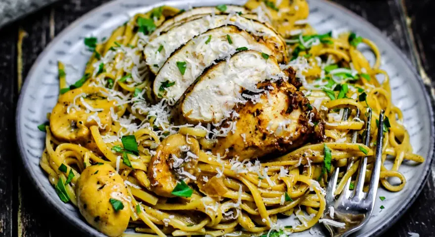 Cremiges Chicken Alfredo mit Pilzen, garniert mit Parmesan und Petersilie. Ein köstliches Gericht, das Lust auf mehr macht.