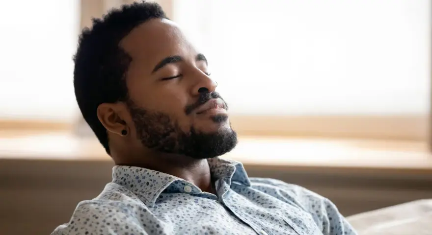 A man with closed eyes and a beard breathes deeply, finding a moment to ground himself amidst the day's chaos.