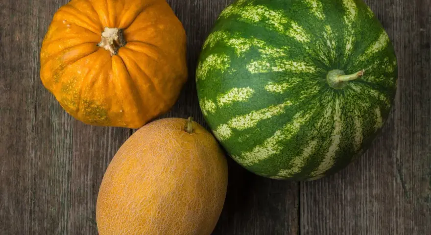 Dynia, melon i arbuz leżą na drewnianym blacie.