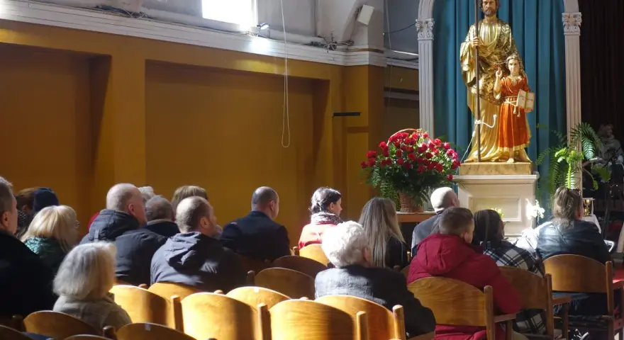Ludzie w kościele, przed ołtarzem z figurą św. Józefa i Dzieciątka Jezus. W tle bukiet czerwonych róż. Sanktuarium Matki Bożej Częstochowskiej.