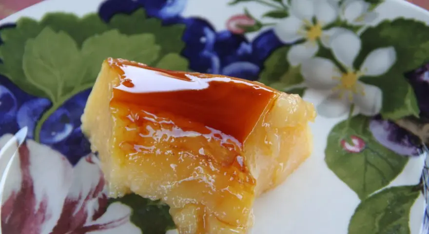 Un trozo de tocino de cielo de la abuela, con su caramelo brillante, sobre un plato decorado con flores y frutos.