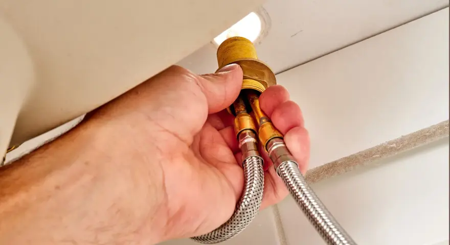 Hands disconnect braided water supply lines from a faucet base, a key step in how to remove kitchen faucet.