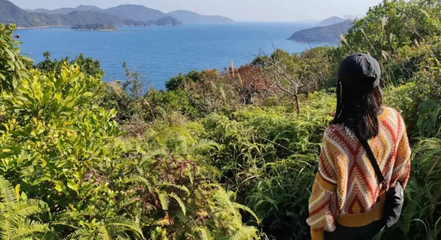 Frauen genießen die Aussicht beim Hong Kong Hiking. Grüne Vegetation und das blaue Meer erstrecken sich bis zu den Hügeln.