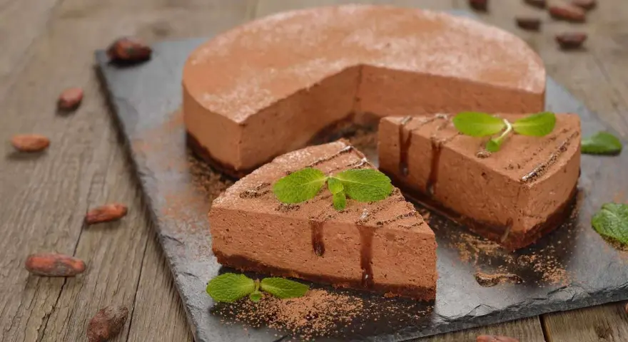 Deliziosa bavarese al cioccolato, spolverata di cacao e decorata con menta fresca. Due fette sono già pronte per essere gustate.